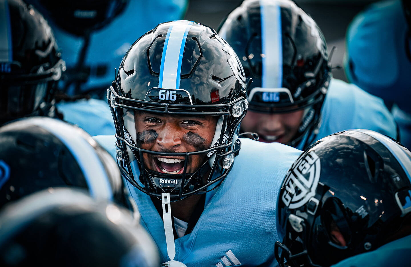 A football player with face paint and a helmet marked "616" shouts intensely during a game, surrounded by teammates in matching uniforms.